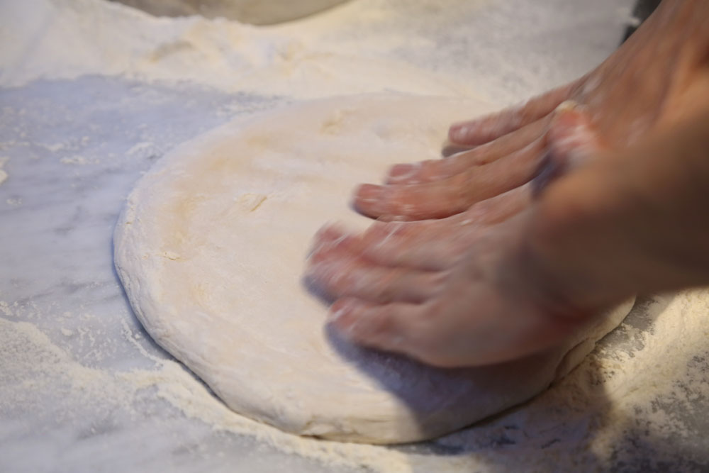 打ち粉をして、円形に成形する。手の平で三角を作るように、指の腹で圧を加えながら伸ばして行く。