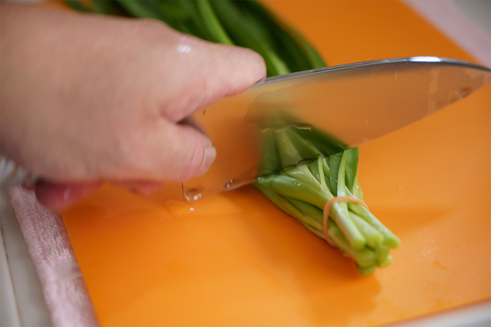 ニラは輪ゴムを付けたまま根元に近い部分を約5㎜切り落とし、30分ほど水に浸ける。ザルに上げて水気を切り、輪ゴムを付けたまま根元側から5～6㎝長さに押し切る。こうすれば片手でもニラがばらけずに切れる。