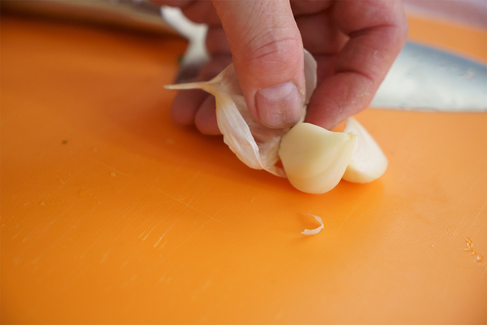 ニンニクを皮ごと縦半分に押し切る。指先で皮を剥き取り、根元を切り落とす。芽は指で取り除く。
