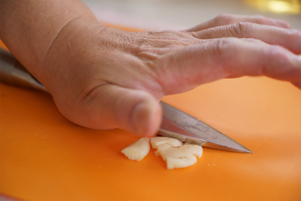 ニンニクに包丁の面を当てて手の平の付け根で叩き潰し、香りを出す。叩き切るように粗みじんにする。