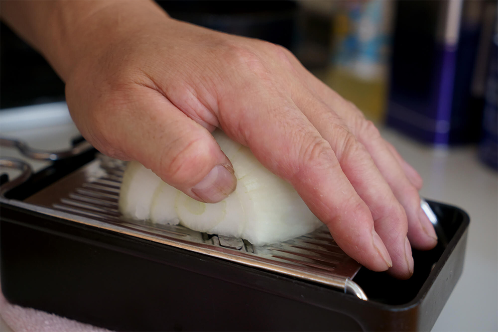 (A)タマネギは縦半分に押し切りにしてから皮を剥いて根元を切り落とす。大きめのスライサーに断面を当ててスライスする。