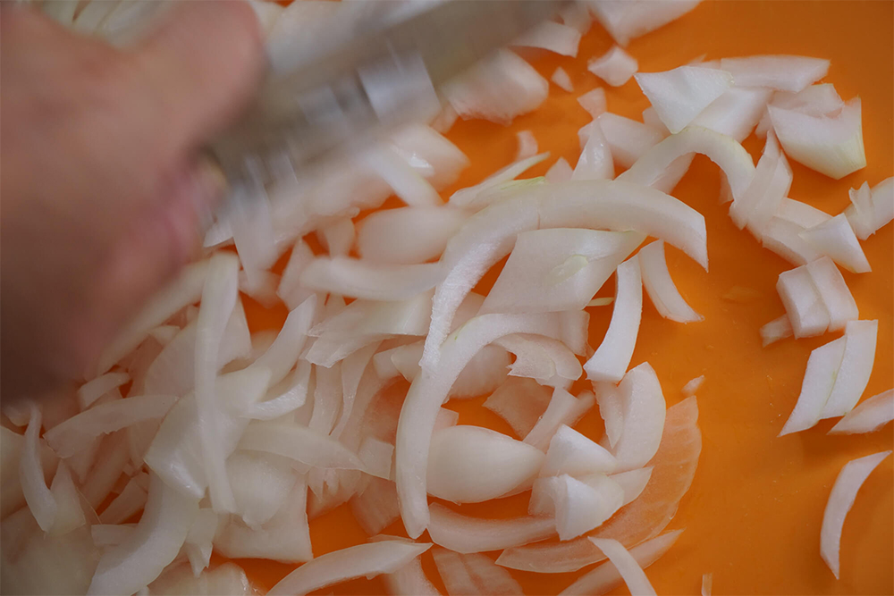 (B)スライスしたタマネギは、包丁で押し切るようにして粗みじん切りにしていく。細かくない方がおいしいと岡田さん。