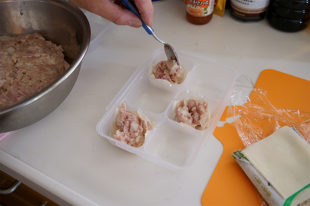 (E)皮は窪みに１つおきに敷き、肉種をスプーンで詰めていく。皮をすべて敷くと、皮が手にくっつくなどして詰めにくい。