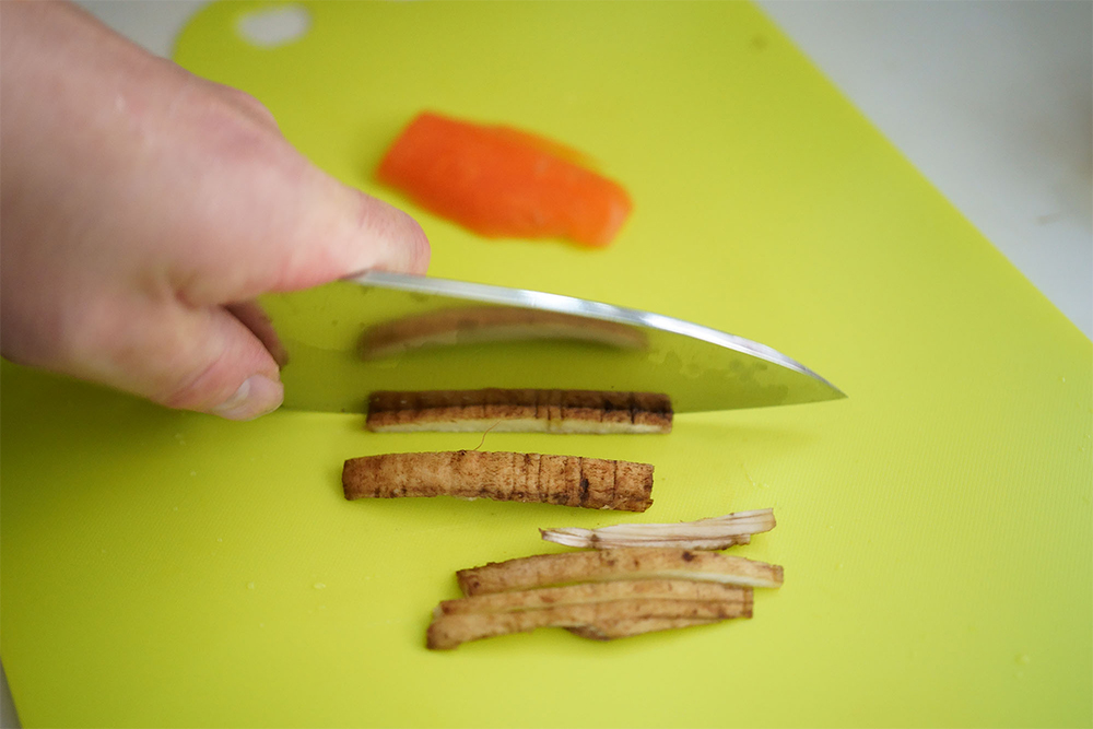 １ 洗いゴボウは６～７㎝長さに押し切りにし、厚さ2.3 ㎜・幅３㎜のせん切り用スライサーにかける。水（分量外）に10分ほど浸けて、途中水を替えてアクと汚れを除き、ザルにあける（A）。