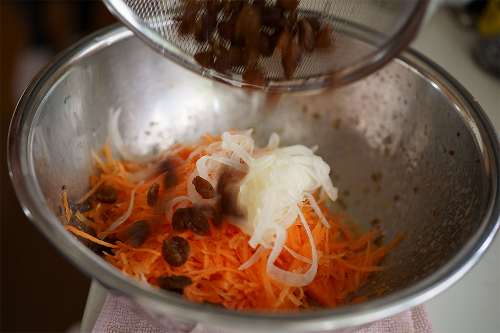 （G）ドレッシングに汁気を絞ったニンジンとタマネギ、レーズンを加えて混ぜる。ラップフィルムを密着させ、５分冷蔵して味を馴染ませる。