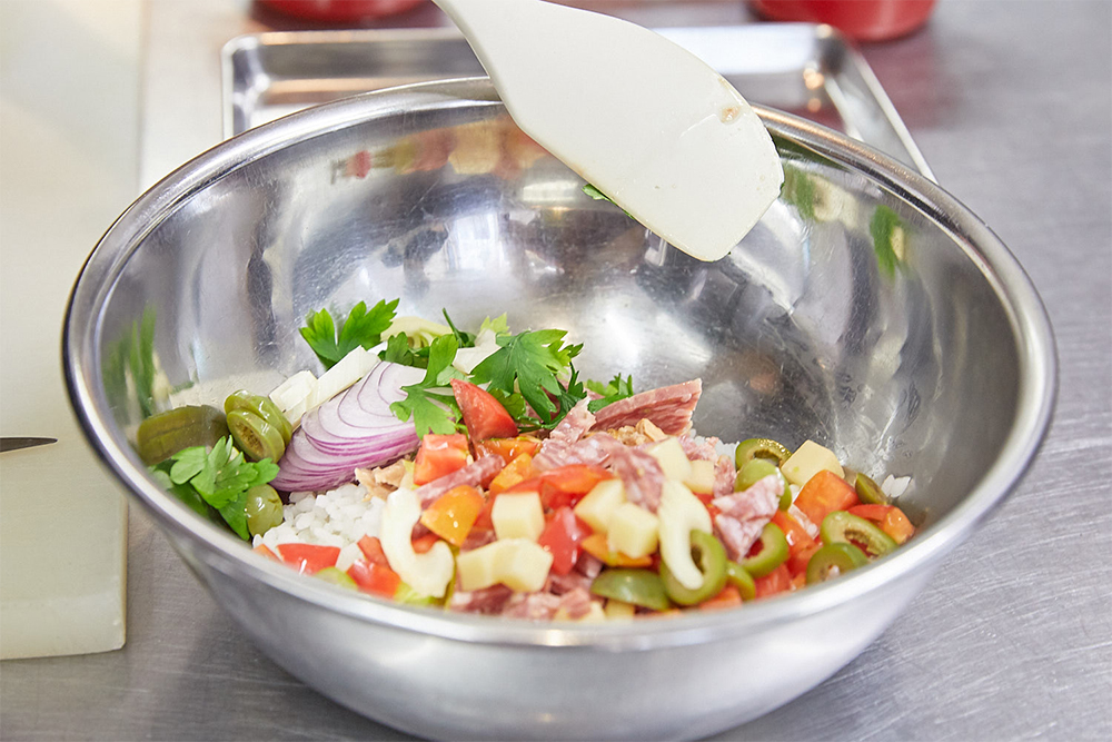 多彩な具材で彩りも豊か。米を赤タマネギやトマト、セロリなどの野菜とツナやサラミ、チーズと合わせて、赤ワインビネガーとオリーブ油、塩で調味。チーズやサラミのコクはありつつも、酸味が効いているので食べ心地は軽やか。