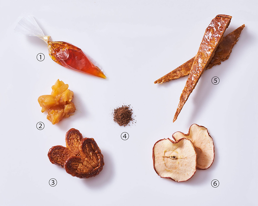 パーツの一つひとつにシェフの丁寧な仕事と磨き上げた技術が光る。①トッピングしやすいよう、ゆるめにのばしたキャラメルソース、②タルトタタン風にキャラメルソテーしたリンゴ、③「アディクト オ シュクル」で販売しているクッキー缶の定番、パルミエ、④バニラのさやを乾燥させて粉末にし、トンカ豆を加えたバニラパウダー、⑤細くカットしたミルフィーユ用のパイ、⑥旬のリンゴをシロップに漬けて乾燥させたリンゴチップ