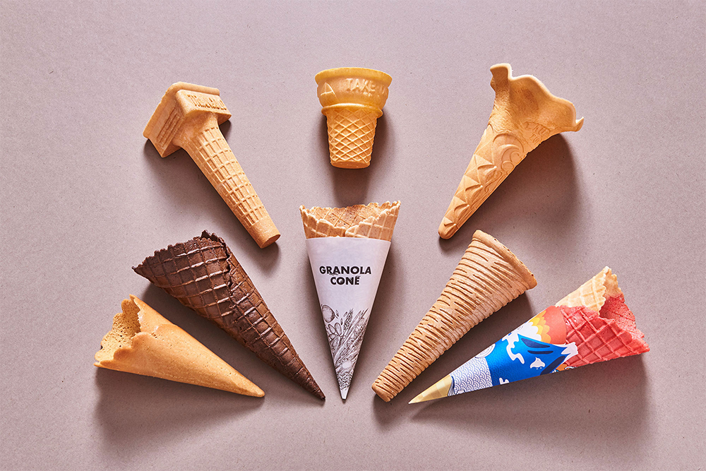 日世のオリジナルコーンは全部で約25種類。お店の雰囲気やソフトクリームのスタイルに合わせて選ぶことができる。 上段左から：ジェラート用に開発された「NO.3 トリアンゴロ?コーン」、平底タイプでポピュラーな「NO.15 テイクアウトコーン」、見た目の美しさだけでなくアーモンドとバターの風味も上品な「ローレルトップ?」。 下段左から：バター風味のサブレ生地をブーケの形に巻いた「ブーケサブレ」、ほんのりビターで見た目もシックな「ココアワッフルコーンS」（石井シェフ使用）、オーツ麦や小麦胚芽を混ぜたヘルシー志向の「グラノーラコーン」、一口目からソフトクリームとコーンを一緒に楽しめるよう作られたスティックスタイルの「クリスピーメープルコーン?」、富士山や着物柄など和テイストのスリーブと合わせて使いたい「紅白ツートンコーン」。