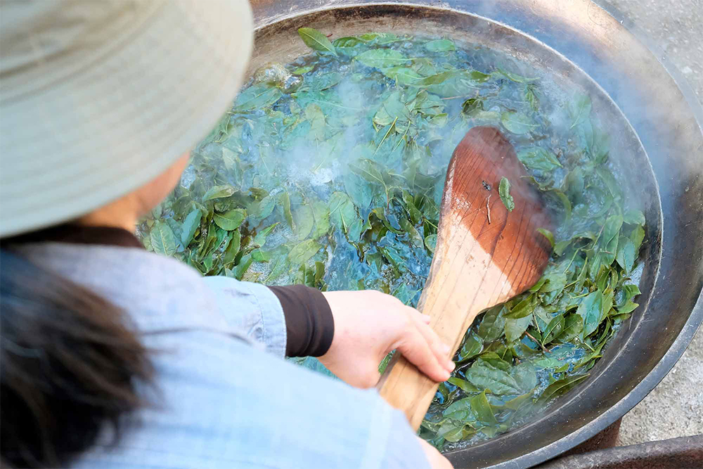 ３．薪をくべて茹でる 茶葉を釜茹でする。杓子を使って上へ下へと混ぜながら、ムラのないよう、均一に茹でる。薪はカシなどの雑木。灰を取っておき、こんにゃく作りで凝固剤に使う。