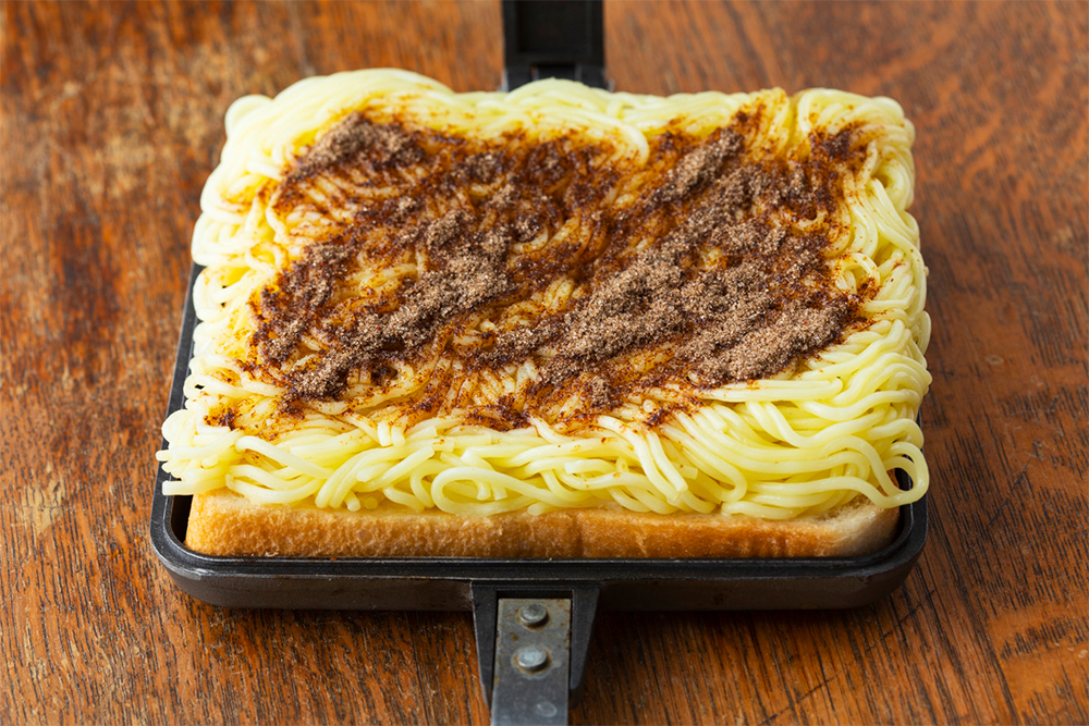 【１】パンの片面にからしとマヨネーズを塗り、塗った面を上にしてバウルーに１枚置く。袋から出した麺をパンの上に収まるようにおき、粉末ソースの２/３をふりかける。