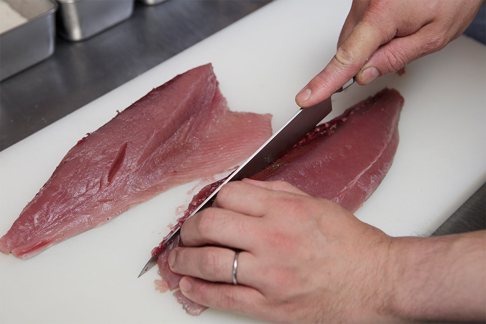 おろしたマグロの半身を縦半分に切り、血合いをとる。皮と身の間に包丁を入れ、滑らせるように皮を引く。