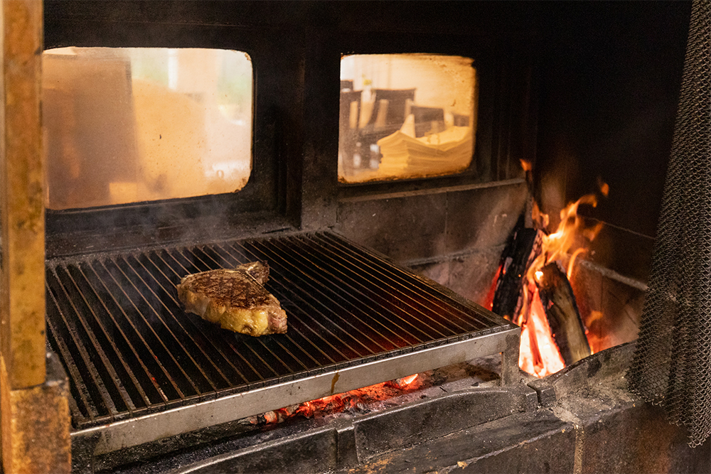 暖炉の右半分の火床で薪を燃やし、熾火になったら、左側の焼き台へ移して食材を焼く。右側は30cmほど深く掘り下げて、炎が焼き台にかぶらないように設計。右側は蓄熱性の高いレンガ、左側は蓄熱しにくいレンガを使用している。