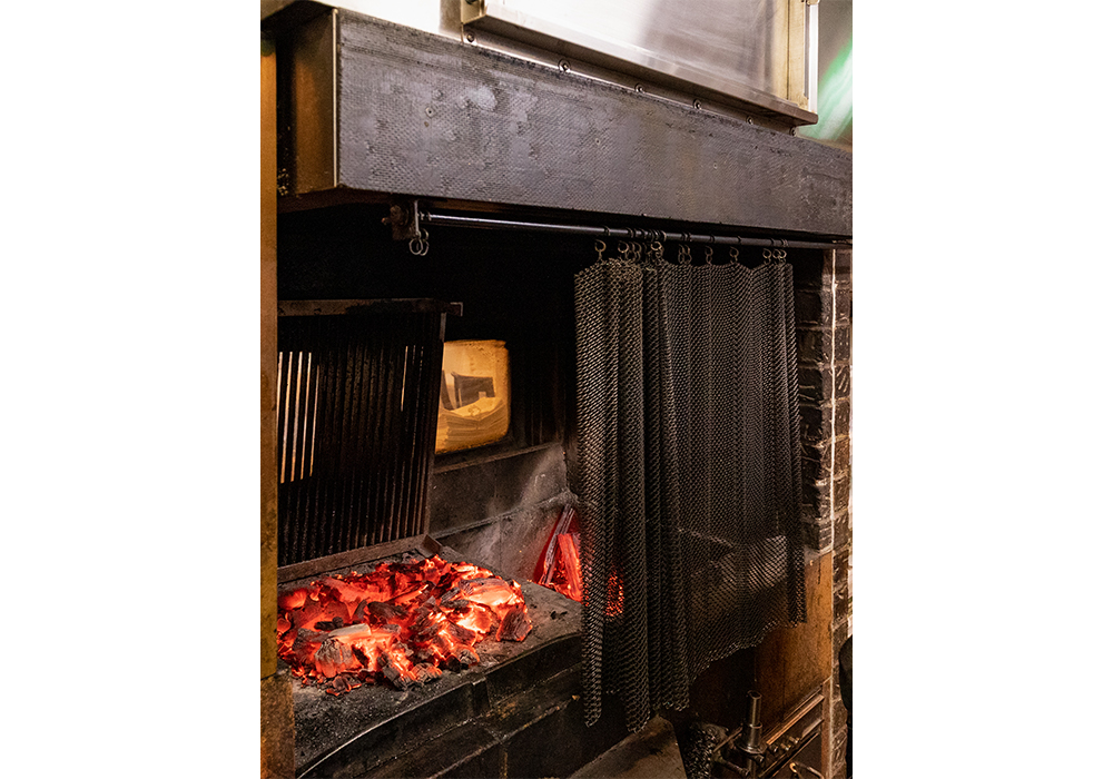 給気と排気の機能も万全。上部にはダクト内にシャワーが流れて油分と煤と熱を取り除く排気システムが格納されている。浄化と冷却を施してから排気されるお陰で都市のビル内でも薪火が使える。また、チェーンカーテンで炎や熱が厨房へ流れ込まないように防御。「Ｆ１のコックピットのような暖炉を目指した」とシェフ。