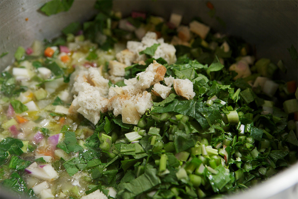 すぐにカブの葉や小松菜などのざく切りと、水に浸して絞ったパンの角切りを加え、鍋底をヘラでこそげ落とすようにかき混ぜる。