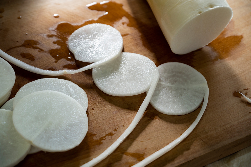 １． 大根をスライスする 直径12㎝ほどの太さの大根を、５～７㎜程度の輪切りにする。写真のように、皮部分が紐になるようにむいてもよい。