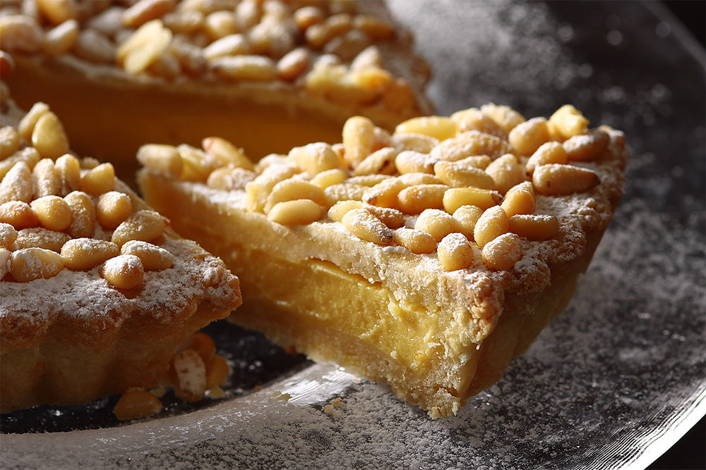 型にタルト生地を敷き、冷ましたカスタードクリームを流し入れ、タルト生地で表面を 覆う。松の実を散らし、180℃のオーブンで１時間焼く。焼き上がりに粉糖をかける。