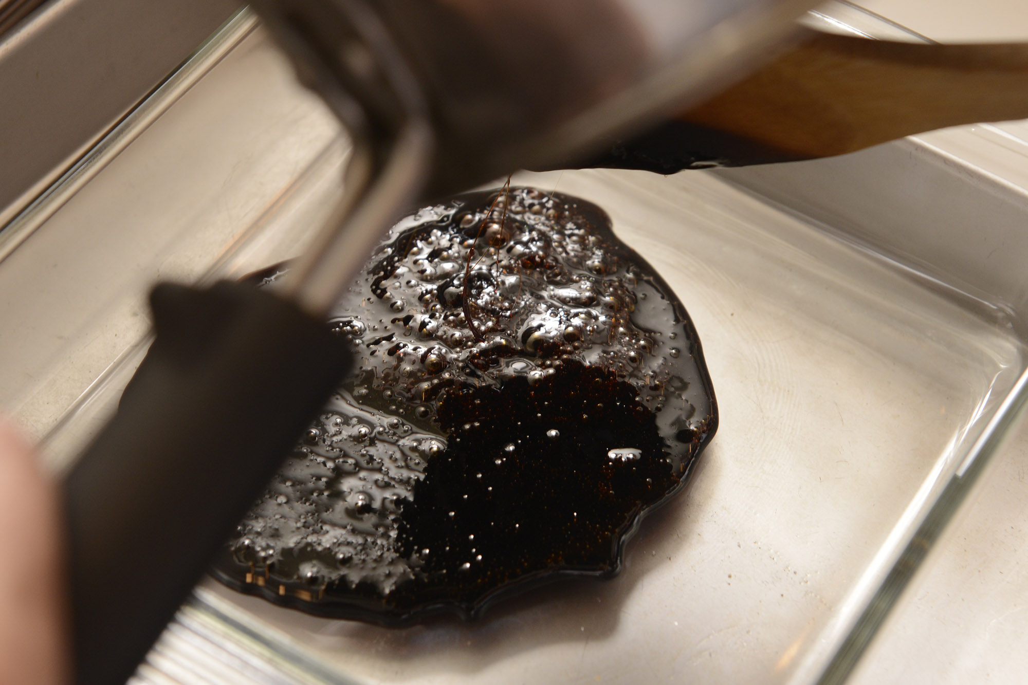 【７】湯せん用のバットの上に耐熱容器を置き、鍋からカラメルを移す。容器を傾けてカラメルを全体に行き渡らせる。 POINT：卵液の水分でカラメルが緩くなるので、硬めの粘度にして容器の底に広げる。