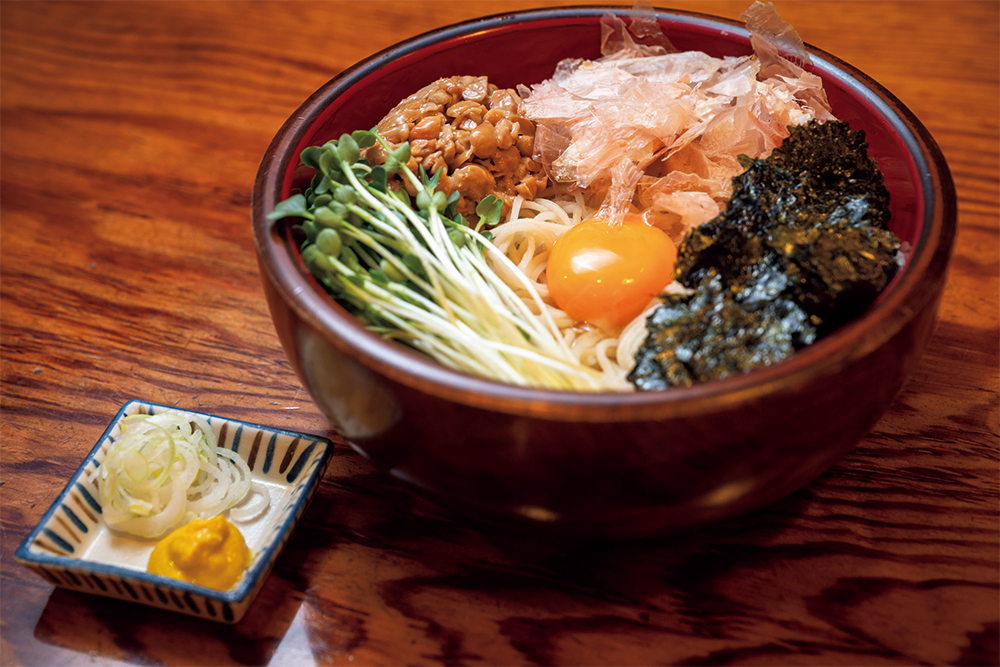 看板メニューの「納豆そば」（￥1,050／税込）は、３代目主人の息子が小学生の時に生まれたメニュー。冷たいそばだが、季節を問わず人気。