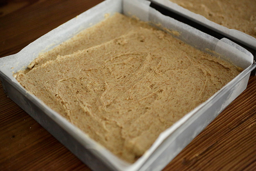 【８】のバター生地をゴムべらでショートブレッド生地の上に移す。小さいL字パレットナイフで型の角まで広げ、表面をざっとならす。 [12]リンゴをランダムに挿す