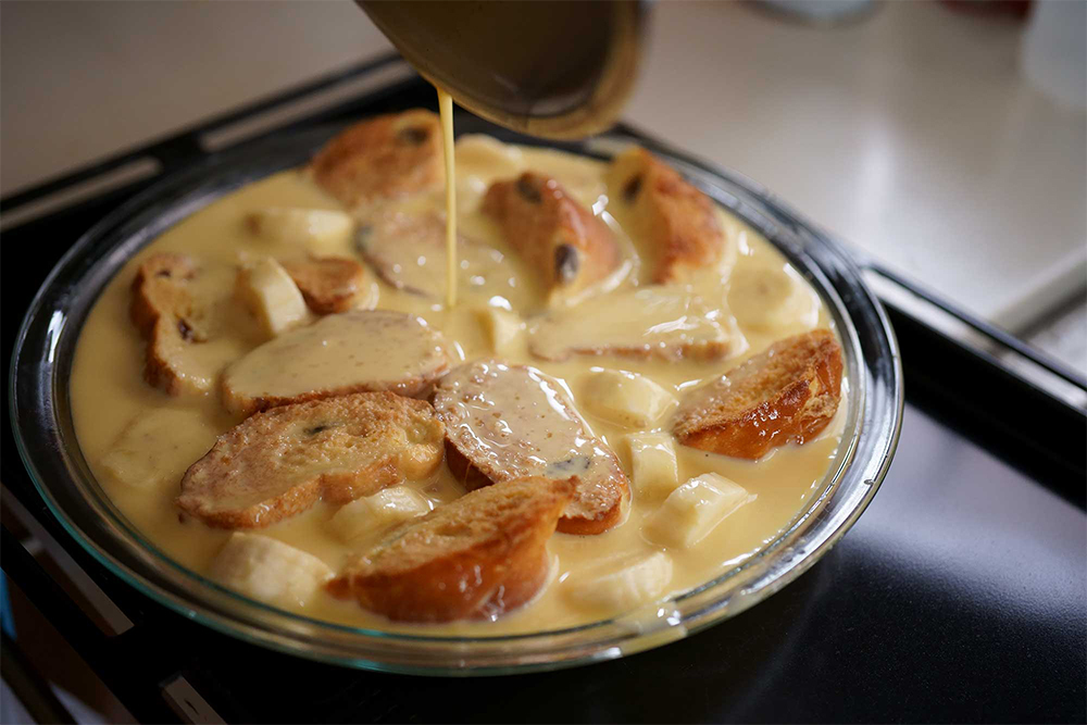 容器を移動してから流し入れる。 プリン種を流し入れるのは、オーブンに設置した天板に型をのせてから。こぼすことなく縁のギリギリまで流し入れられる。パンをクロワッサンにして焼成するとパンと卵液の食感の差が際立ち、柔らかいパンでは卵液とパンが一体化する。