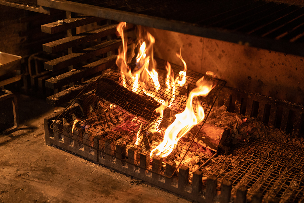 鋼鉄製のフレームは太くて堅牢。炉床はなく、フレームと同素材の棒が並んだ上に目の細かい焼き網を置いて薪を燃やす。隙き間から落ちる灰を下の引き出しが受ける、という構造。暖炉メーカーと幾度も修正を重ね、現在の形に至った。
