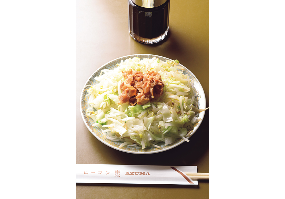 炒めた白菜とキャベツ、モヤシの上に甘辛い醤油だれで煮た豚バラ肉をトッピングした「焼きビーフン 並」はランチのみで提供。テーブルに運ばれてから、好みでニンニク醤油をかけるスタイルも東流。