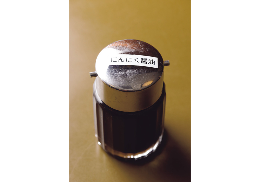 ＜秘密のにんにく醤油＞ 店のテーブルには、ニンニクを醤油、日本酒、砂糖と合わせた「にんにく醤油」が置かれている。焼きビーフン、汁ビーフン共に、これをお客の好みでかけて食べる。ご主人によれば「風味づけに、ほんの少量かけるのがベスト」。作り方は、残念ながら非公開。店の味を確かめてから、上記の材料で是非、挑戦してみてほしい。