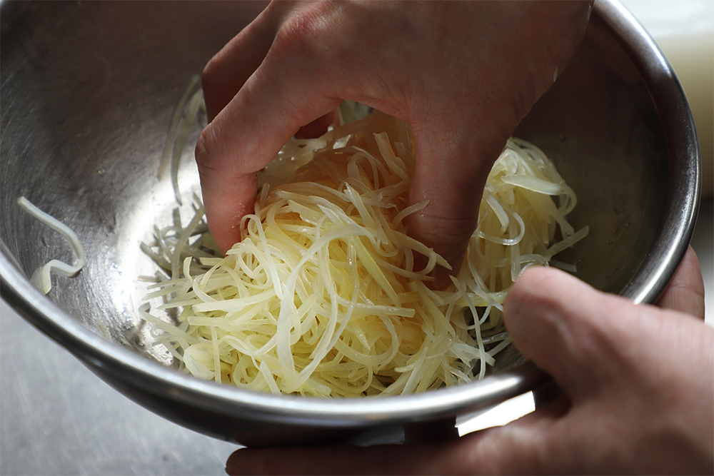 熱が取れたらザルに上げ、ひとすくいずつ手で絞る。 POINT：水気が残っていると味がボケる。ジャガイモが折れないように注意して絞る。 ［５］完成