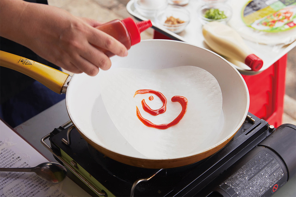 中火のフライパンにライスペーパーをのせる。熱で浮き上がってくる前に素早くチリソースを塗る。 [２]残りの具材をのせる