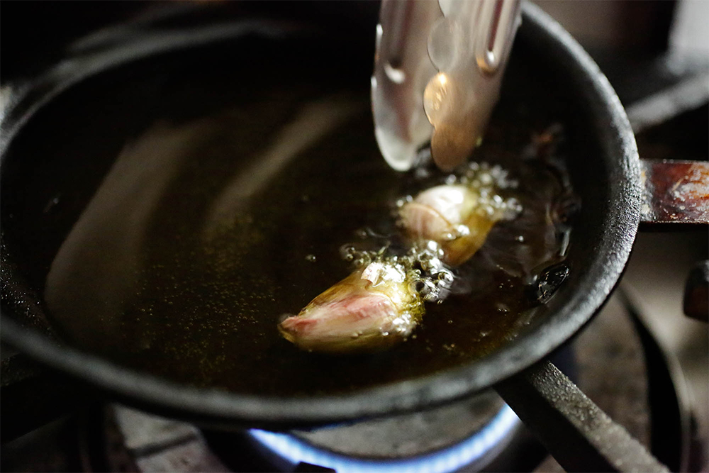 [１]オイルとニンニクを火にかける 小さめのフライパンにオリーブ油とニンニクを入れ、弱火にかける。