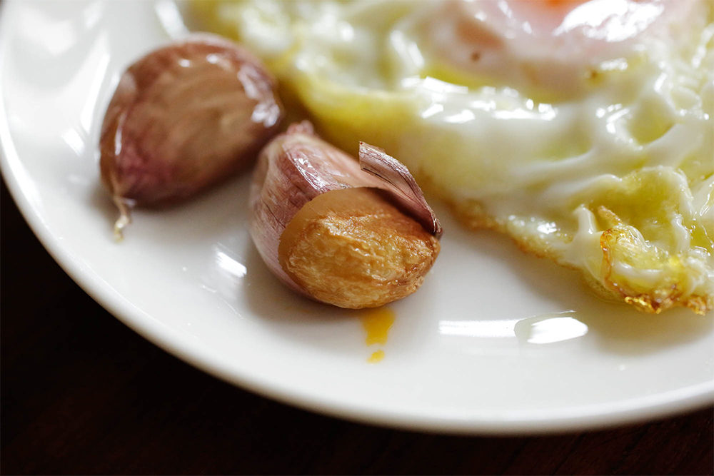 皮付きのままでゆっくりニンニクを加熱すると、みじん切りやスライスにしたニンニクとは違った奥ゆかしい香りが引き出される。ニンニクは皮の中で蒸し焼き状態になり、最後はホクホクとしたイモのような食感に。残ったオイルのほうも他の料理に展開する。 ＜食べ方＞