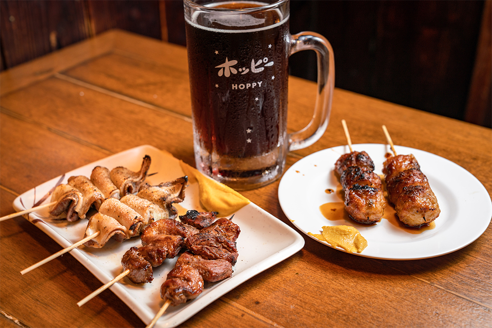 黒ホッピー（480円）と焼鳥。焼鳥は全21種類で、各２本から注文可。モツは芝浦から仕入れた新鮮なものを使用している。佐藤さんは、店で３杯、家で２杯飲むのが定番。