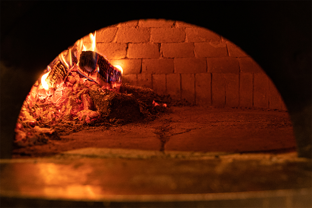 火の核ができたら、ナラ材（火力が安定して強い）を投入。内壁を舐めるように炎が立ち上がり、熱の対流を起こして窯内を温めていく。