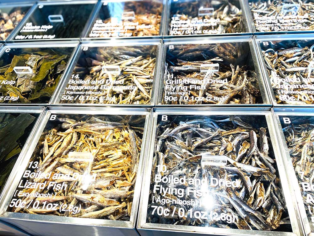 （写真）多彩なだし素材をスタイリッシュに並べたショーケース。各素材の産地の思いに耳を傾けたり、その場で粉砕・包装するカスタムメイドのだしパック工程に熱心に見入るお客もいるといい、反応は上々だ。