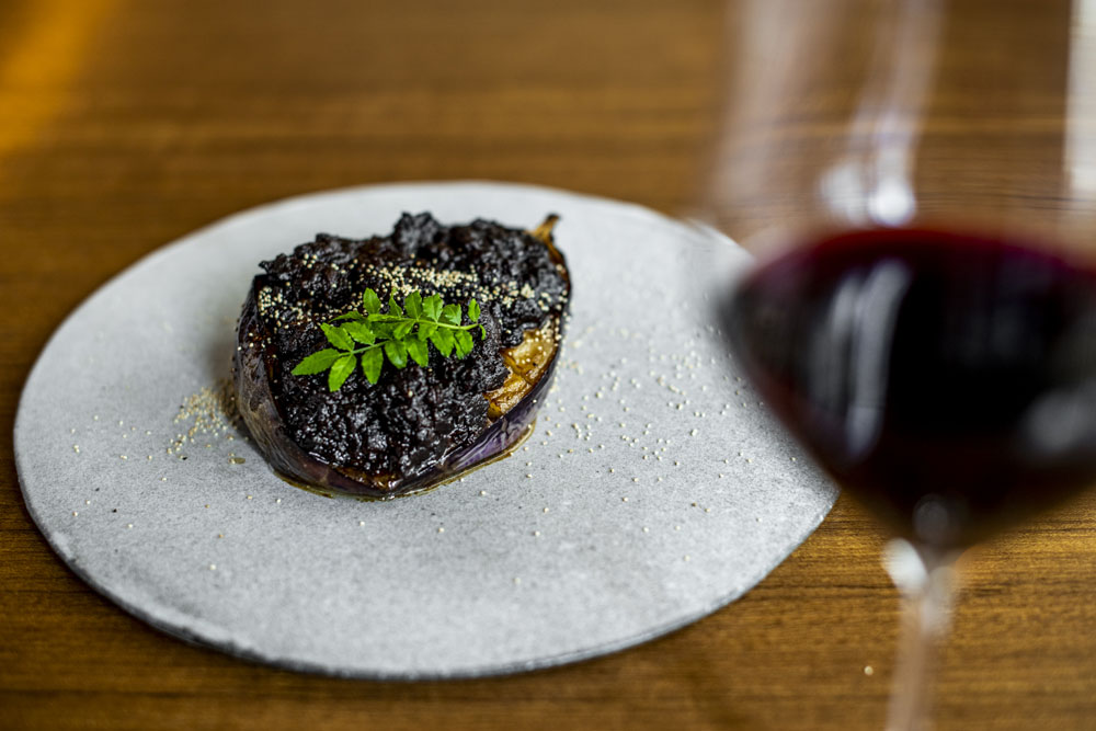 料理：「米ナスの鴨味噌田楽」 赤味噌と練りゴマを合わせた田楽味噌に粗く刻んだ鴨のそぼろをたっぷり加え、オーブンでじっくり焼いた米ナスに絡めて食べる。ケシの実と山椒の葉をアクセントに。
