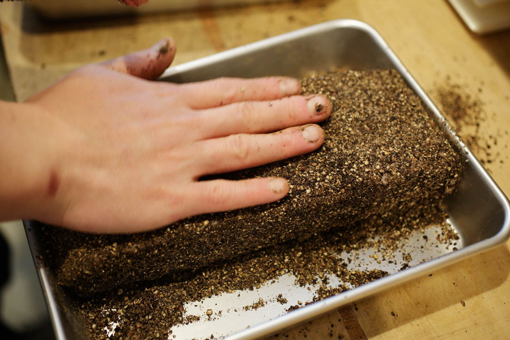 バットに細かく挽いた黒コショウをたっぷり用意し、肉を置く。手の平で押さえながら表面全体を覆う。