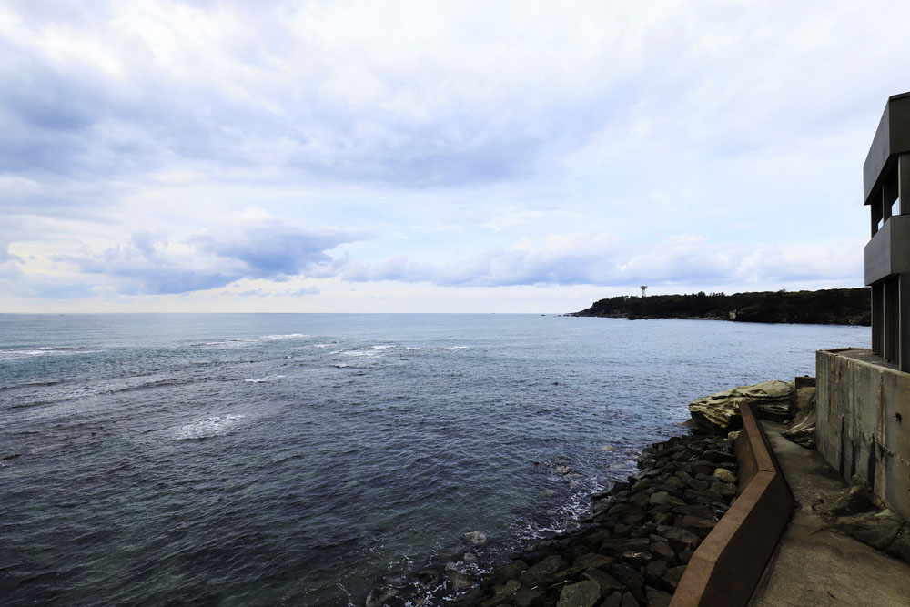 旅館名のとおり、手が届きそうな眼前に日本海を抱くロケーション。外壁には塩害に100年耐性をもつとされるコンクリートを使用している。奥に見える岬は東尋坊。