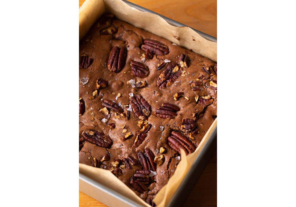 チョコレートのほろ苦さ、ブランデー漬けプルーンのコクと酸味、ピーカンナッツの香味が三位一体となった大人のブラウニー。表面のおいしそうな艶は、グラニュー糖を使うことによって生まれる。