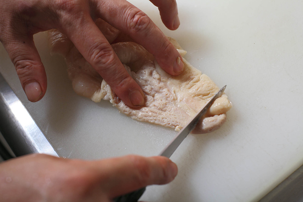 刃先でモツの表面の白い汚れをこそげ落とす