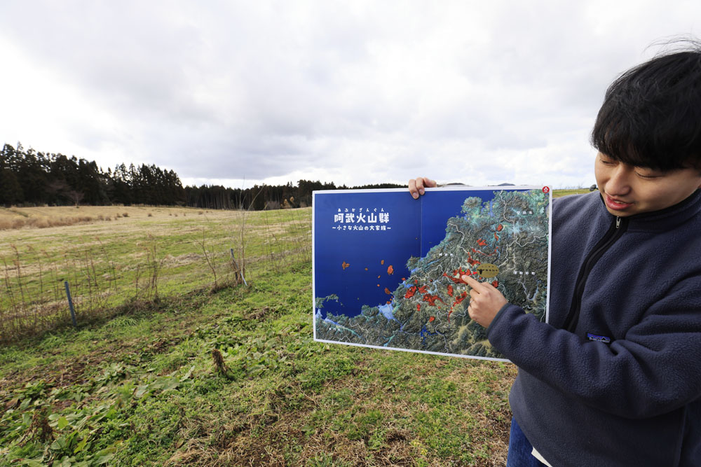 放牧地をバックに阿武町一帯の地形や地質について解説する藤尾さん。春になると、妊娠牛がこの放牧地に放される。