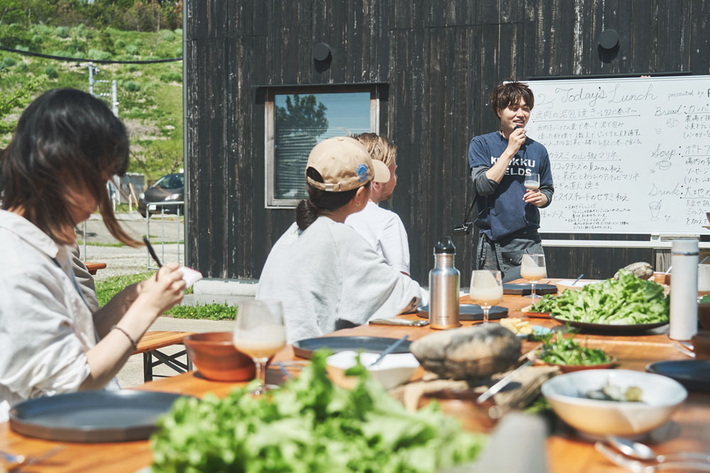 山名シェフが料理解説。ホワイトボードにはメニューと共に食材の素性が記されている。場内産・地元産の食材ばかり。泥包み焼きの鹿肉もソーセージのイノシシも木更津の猟師が獲ったジビエ。