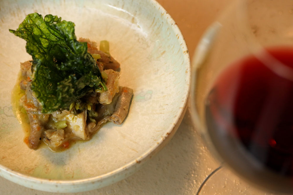 モツ煮と赤ワイン。「群馬県民はモツ煮をよく食べる。蕎麦屋の小鉢でも登場するほど」。モツをニンニクと炒め、ソフリットで煮込んだ。薪火グリルで蒸し焼きにしたカブと合わせ、素揚げの葉ワサビを添えて。屠畜したてのモツを分けてくれる精肉店が隣町の沼田市にある。
