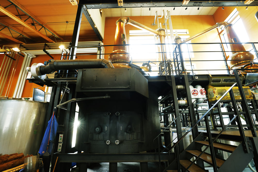 蒸溜所のシンボルでもある直火式の単式蒸溜機。胴体部にある薪を燃やすための窯は、ピザ窯職人に依頼して特注で制作されたもの。「強いボディと甘味、香ばしさ、長い余韻。蒸気の蒸溜とは明らかに違う味わいの個性も魅力」と中村さん。