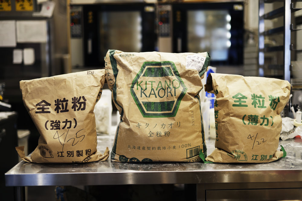 全粒粉は３種類を使用し、植物性の素材の組み合わせに、穀物の旨味を加える。（左から）バゲットに使う十勝産はるきらり全粒粉（江別製粉）。食パンなどに使う北海道産キタノカオリ全粒粉（アグリシステム）、ドーナッツに使う福岡県産シロガネ小麦の薄力粉の全粒粉（江別製粉）。
