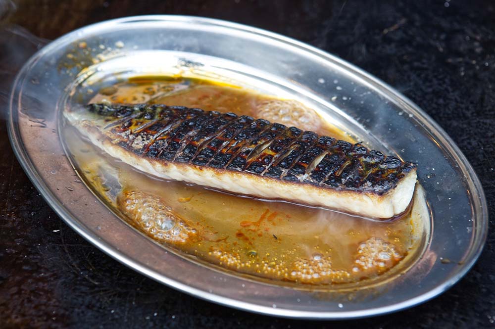（写真）新鮮なサバは強い炎で皮目をさっと焦がしてからソースと一緒にステンレス皿にのせ、熾火の上で熱して香りを立てる。