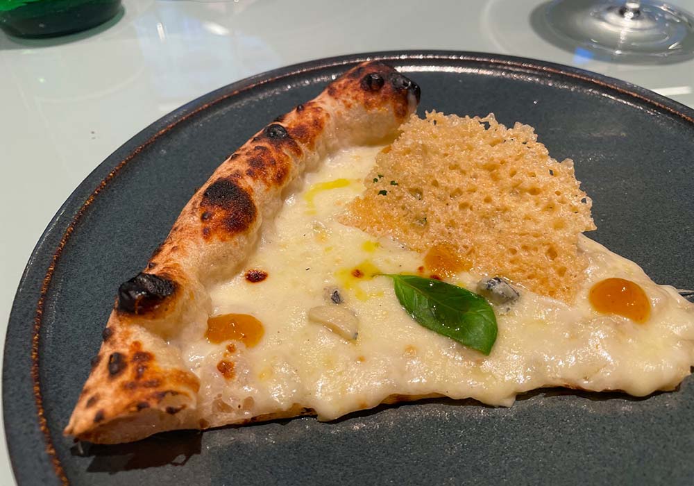 （写真）「ボトックス（Botox）」とネーミングされたピッツァ。乳牛のモッツァレッラ、熟成したカチョカヴァッロ、水牛の青カビチーズなど、数種のチーズで作るフォンドゥータソースに、苦味を感じるサレルノ産レチーノ種のE.V.オリーブ油を合わせ、濃厚な甘味のチレント産白イチジクのコンフィチュール、パルミジャーノ・レッジャーノのチップスを添えた。名前の由来は「食べると気持ちが和らぎ、顔立ちも穏やかになり、美容施術を受けたようになるから」。