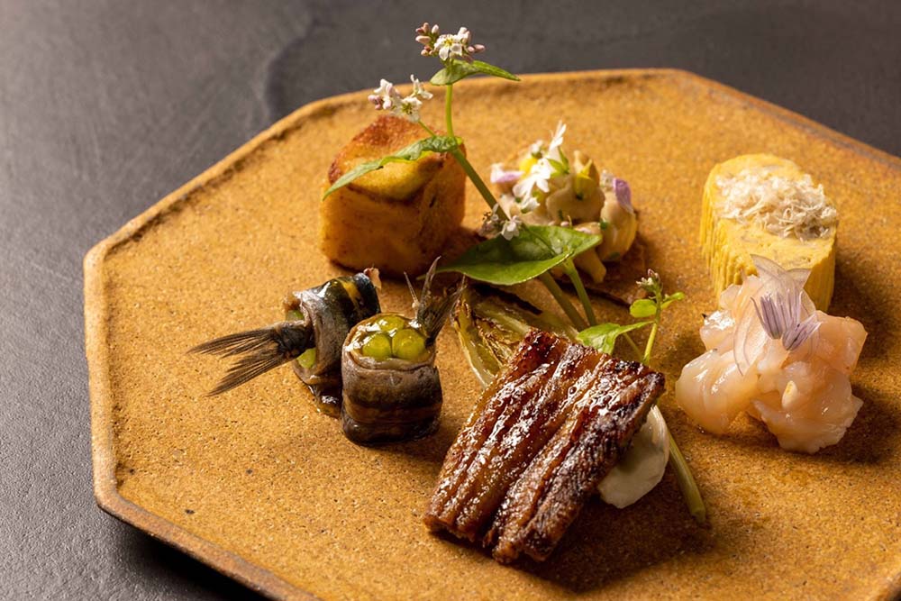 （写真）前菜の盛り合わせ。左奥から時計回りに：ウサギのコロッケ。ペレチコスと呼ばれる旬のキノコはフレッシュで。軽く炙った卵焼きの上には鰹節ならぬ鶏胸肉の削り節。軽くスモークした昆布の香りのエビ。ウナギの蒲焼はシェリービネガーと。アンチョビーはスペインのタパス「ヒルダ」を思い出させる。