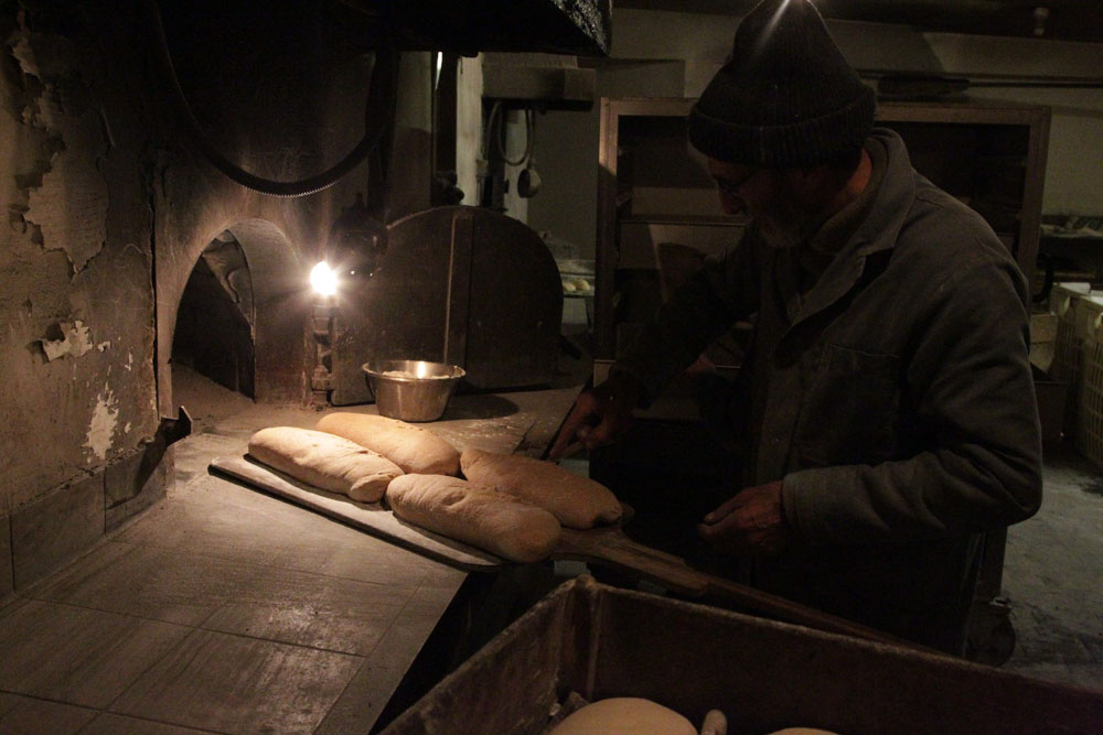 白くなるまで焼いた柴を取り除き、濡れた麻布で窯内の温度を下げた後、生地を窯の奥から半円状に置いていくセルジュ・エネ。窯入れ前に、ナイフでクープを入れる。