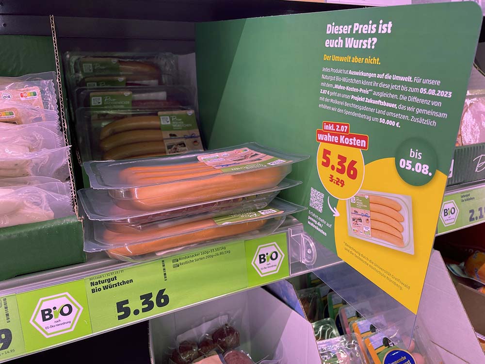 （写真）興味深いのは、オーガニックやヴィーガン製品の値上がり率。オーガニックのウィンナーソーセージは通常価格3.29ユーロに、気候0.56ユーロ、水0.11ユーロ、土地0.79ユーロ、健康0.61ユーロが加算されて5.36ユーロとなり、値上がり率は62%。