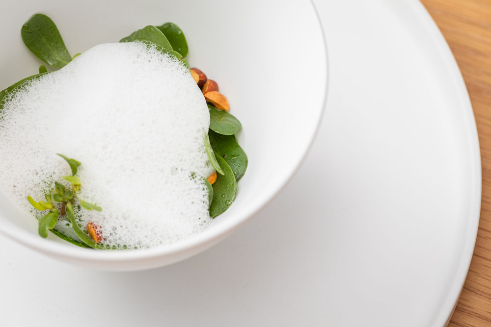 「帆立貝のポワレ 小松菜のフランと貝のエキューム」。ホタテとアサリのだしにバターを加えた泡のソースにもヘーゼルナッツオイルを香らせた。